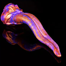 Load image into Gallery viewer, An extra terrestrial creature dildo with a long tongue in ombre color of gold and purple suctioned to a black marble wall.