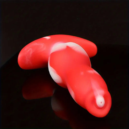 A red and white ombre dog penis anal plug sex toy laying down on a black shiny bench.